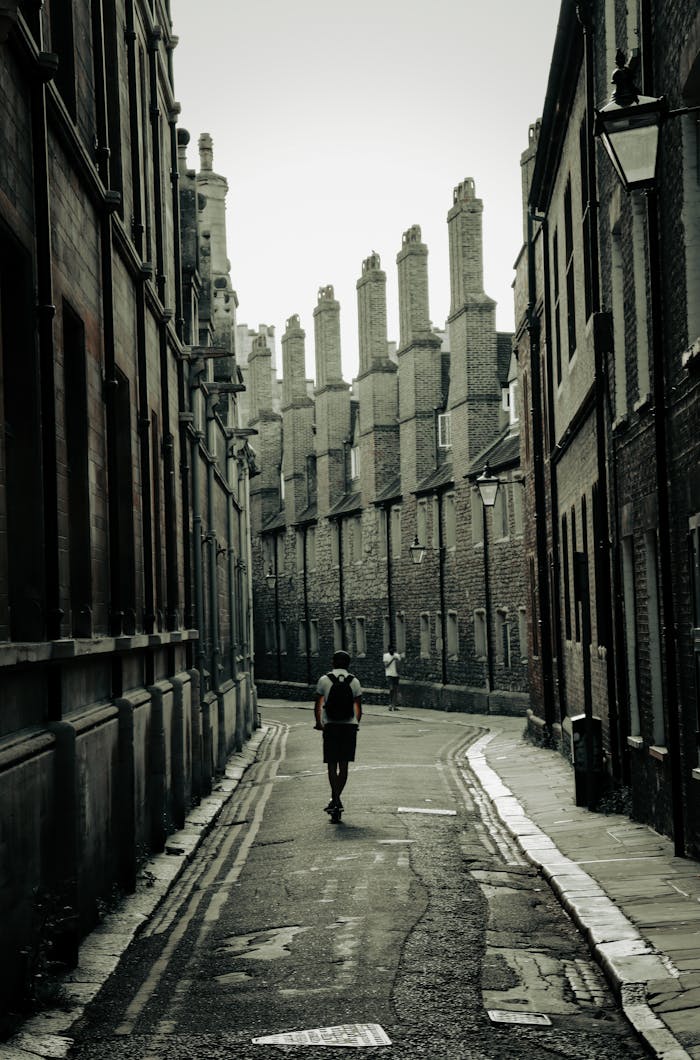 A solitary figure walks down a historic street in Cambridge, showcasing classic architecture.